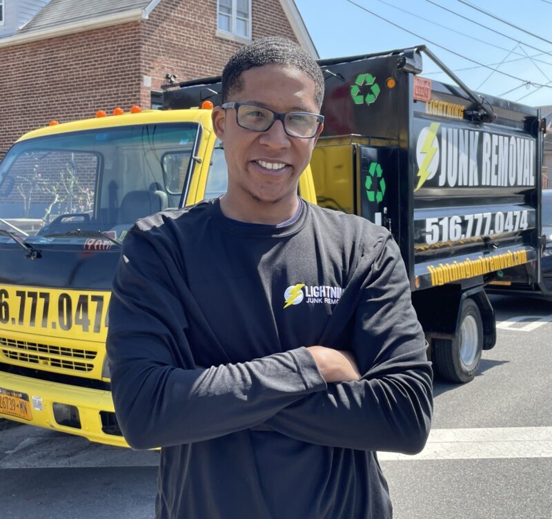 Junk removal professional smiling in front of their truck parked in the Bronx
